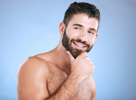 Idea, beauty and natural with a man model in studio on a blue background for skincare, wellness or grooming. Face, beard and skin with a handsome young male thinking about cosmetics or treatmentの写真素材