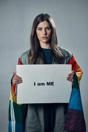 Woman, protest and poster in pride for gay, LGBTQ equality or human rights against gray studio background. Portrait of confident female activist with I am me message board for sexuality empowermentの写真素材