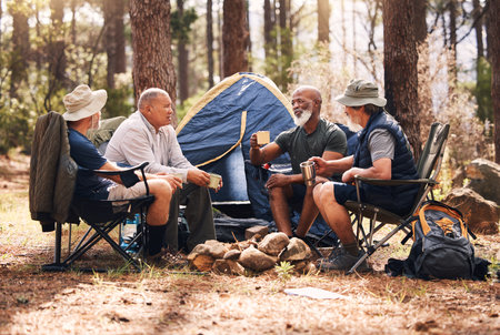 Man, friends and camping in nature with coffee for travel, adventure or summer vacation together on chairs by tent in forest. Group of men relaxing, talking or enjoying natural camp by trees outdoorsの写真素材