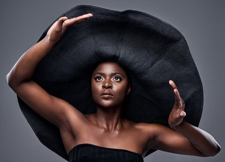 The wider the brim, the more protection you receive. a young woman wearing a oversized sunhat against a grey background.の写真素材