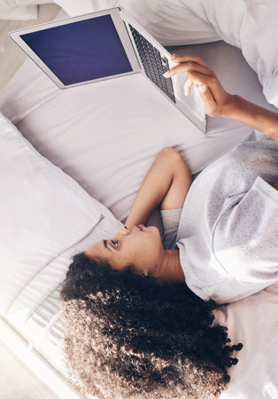 Lazy, sad and woman lying down with a laptop watching or streaming movie, website or app in a home, house or apartment. Rest, break and young black female using in internet subscription to relaxの写真素材