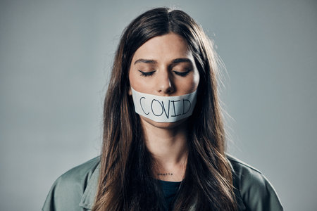 Woman, tape and mouth with silence for protest, social activism and fight against covid 19 by background. Human rights, gen z girl and studio with healthcare opinion for freedom, choice and visionの写真素材