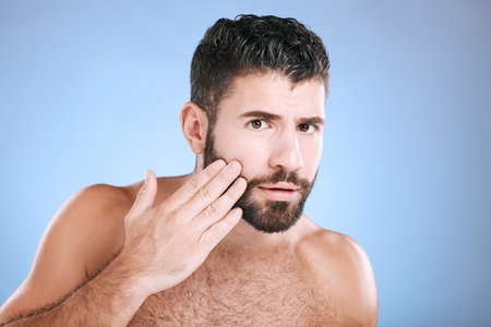 Skincare, beard grooming and portrait of man on blue background for beauty, wellness and salon. Luxury spa, dermatology and worried male check face for healthy skin, blackhead and facial hair growthの写真素材