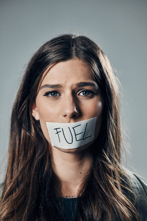 Woman, face and tape on mouth for fuel prices, ecumenic struggle or financial crisis against gray studio background. Portrait of female activist with covered lips in silence, speech or voice messageの写真素材