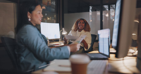 Business women, documents and collaboration with partnership and paperwork, working together in office. Partner, conversation and planning with paper, coworking at desk and computer, online and help.の写真素材