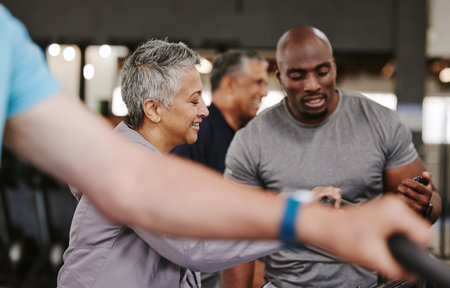 Senior group, exercise bike and personal trainer for fitness, time and retirement wellness by blurred background. Elderly woman, bicycle training or diversity with black man, stopwatch and motivationの写真素材