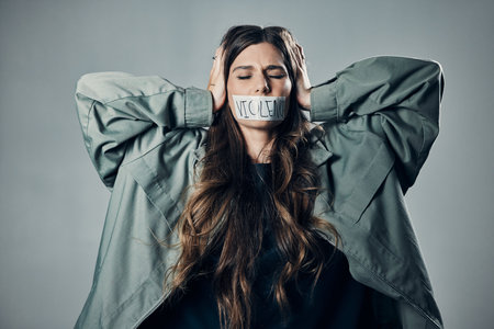 Woman, protest and tape on mouth in fear for cold war, armageddon or doomsday against gray studio background. Female activist with hands on head and message to stop or end global violence in societyの写真素材