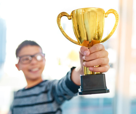 One of many more awards to come his way. an intelligent young boy proudly holding his academics trophy at home.の写真素材