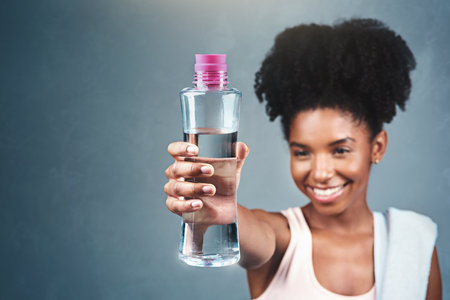 Drinking sufficient water boosts your metabolism. a sporty young woman holding up a bottle of water.の写真素材