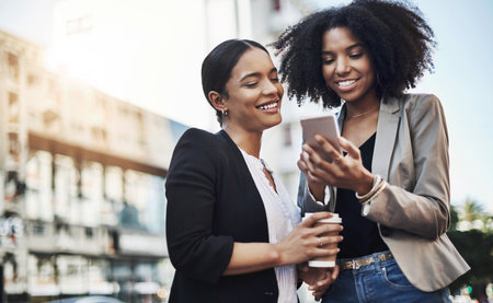 Heres what the client just said. two businesswomen looking at something on a cellphone in the city.の写真素材