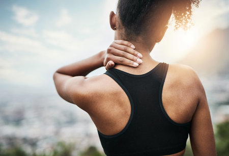 The strain is starting to reach her neck. Rearview shot of a sporty young woman holding her neck while exercising outdoors.の写真素材