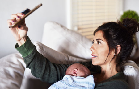 Selfie with my child. a cheerful young woman lying on the sofa while holding her little infant son and taking a selfie at home during the day.の写真素材