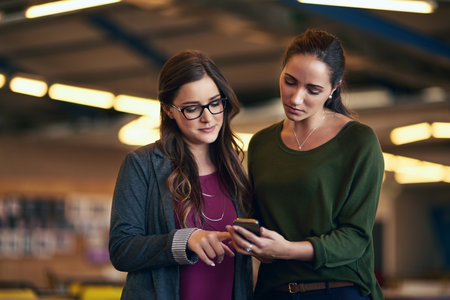 Can you help me figure this out. two businesswomen discussing something on a cellphone.の写真素材