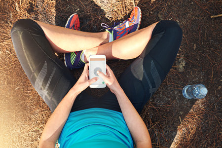Planning her run. a sporty young woman using her cellphone while out in nature.