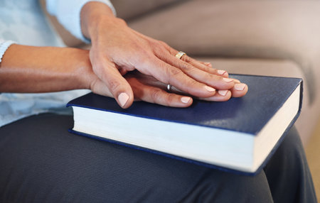 Bible, prayer and hands of old woman in living room for religion, book and Christian faith. Spiritual, God and worship with senior lady praying with holy text at home for wellness, believe and goalの写真素材