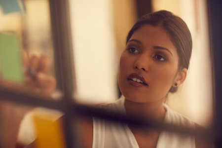 Glass walls are a great place to jot down ideas. a young attractive businesswoman brainstorming on a glass wall in the office.の写真素材