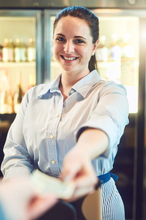 Thank you Come again soon. Portrait of a young woman receiving payment from a customer in a cafe.の写真素材