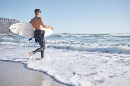 Surfing, man and walking in waves, sea and ocean of summer, freedom and blue sky mockup in Cape Town. Surfer guy, board and swimming in water, beach and relax on holiday, travel or sunshine adventureの写真素材