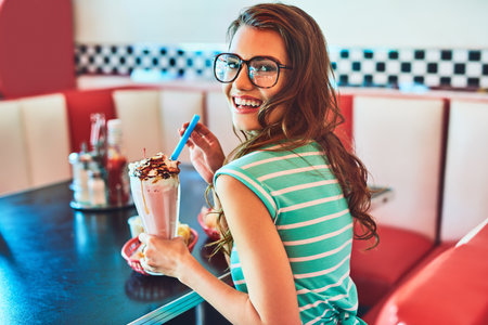 The milkshakes here are delicious. Cropped portrait of an attractive young woman enjoying a milkshake in a retro diner.の写真素材