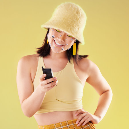 Asian woman, texting and studio with beauty, fashion and eyes sticker art on face with smile for...