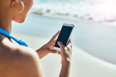 Summer, the season for sharing on social media. a young woman using a mobile phone at the beach.の写真素材