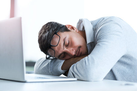 Nobody will notice if I take a quick nap...a young businessman sleeping at his desk in an office.