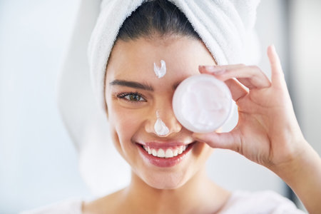 Radiant skin starts with good quality products. Portrait of a beautiful young woman applying moisturizer to her skin in the bathroom at home.の写真素材