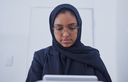 Muslim, tablet working and hijab of a serious woman employee from Dubai writing code. Islam, web data and coding program of a it worker in a office planning with business software and analyticsの写真素材
