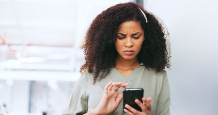 Phone, black woman and frustrated frown of a person on digital communication reading fake news. Annoyed woman on web, internet and social media scroll confused about digital media reading in a officeの写真素材