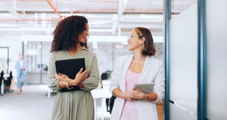 Creative business woman, tablet and walking in discussion, laughing or joke together at office. Happy women employee designers having a walk for social or funny conversation in startup at workplaceの写真素材
