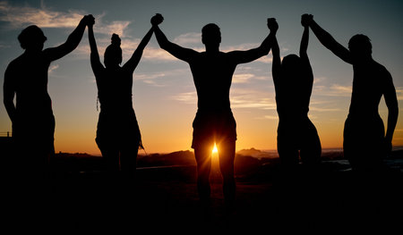 Friends, celebration and holding hands on sunset beach silhouette, nature freedom or community trust support. Men, women and people sunrise shadow in solidarity, team building or travel bonding goalsの写真素材