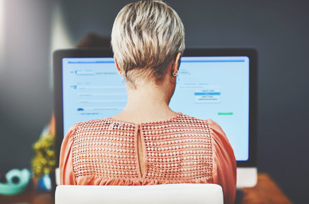 Working on creating her own success. Rearview shot of a young businesswoman working on a computer in an office.の写真素材