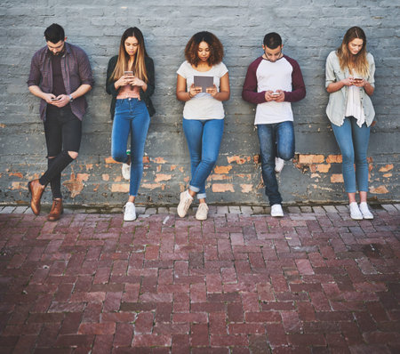 The 4g generation. a group of young people using their wireless devices together outdoors.