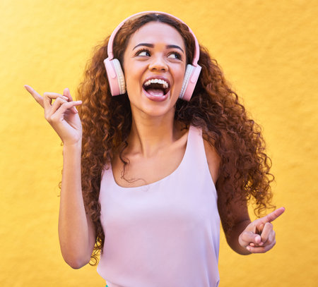 Music, thinking and dance with a black woman listening to the radio outdoor on a yellow wall...