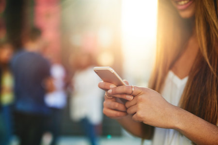 Time for a status update. an unrecognizable young woman sending a text message while standing outside.の写真素材
