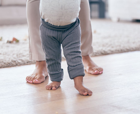 Baby feet, walking and learning with mother in a living room lounge with mobility development. Floor, home and first steps of a young kid with mama together with love, care and support in a houseの写真素材