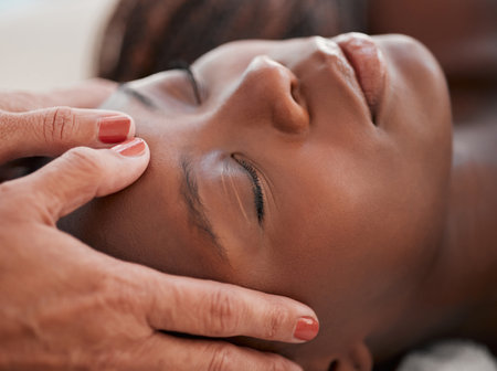 Skincare, beauty and black woman getting a facial massage for health, wellness and self care. Cosmetic, spa and calm African female sleeping while doing a luxury natural face treatment at a salon.の写真素材
