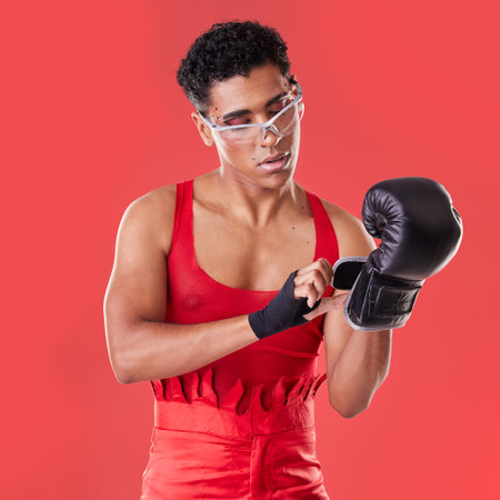 Gay man, studio and boxing glove on hand with punk costume, makeup and lgbt aesthetic by red background. Young bodybuilder, gen z fighter and fitness with strong body, self care and pride for boxerの写真素材