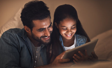 What better way to bond than with digital bedtime stories. a father and his daughter using a digital tablet together at bedtime.の写真素材