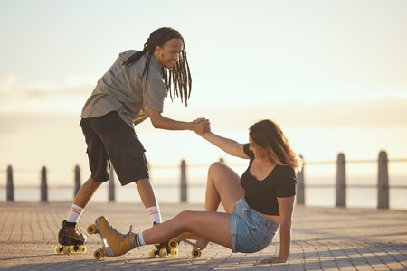 Help, falling and couple roller skating and holding hands at the beach in summer for a fun and healthy cardio activity. Friends love to skate and exercise on sidewalk as girl falls on the groundの写真素材