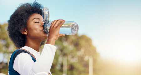 Sports, black woman and drinking water at field for training, exercise or match against mockup. Hydration, fitness and thirsty athletic girl relax with drink during workout, practice or outdoor gameの写真素材