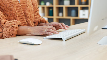 Closeup of woman hands typing on a keyboard while sitting at a desk and sending an email in a modern...