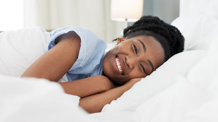 Sleep, bed and relax with a black woman sleeping in the bedroom of her home and dreaming. Resting, relaxing and peace with a young female lying on a pillow and under a duvet in a house in the morningの写真素材