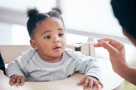 Food, breakfast and parent feeding a baby in the morning while eating porridge with a mother. Hungry, feed and African child ready to eat a meal, lunch or dinner with a mom in a family homeの写真素材
