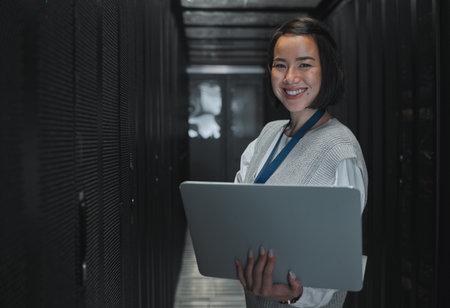 Woman with laptop, server room and information technology, smile in portrait with engineer and datacenter Software update, cybersecurity and network with Asian female setting up firewall and databaseの写真素材