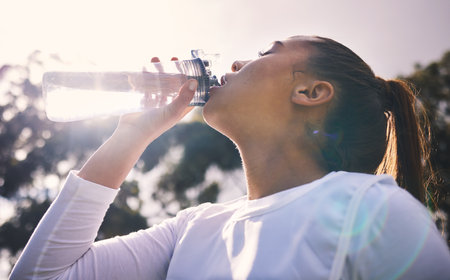 Drinking water, fitness and running with a sports woman outdoor for a cardio or endurance workout. Training, exercise and wellness with a female athlete taking a drink for hydration on a breakの写真素材