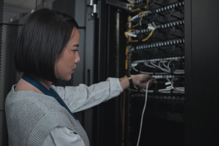Asian woman, technician and server room for cabling, networking or system maintenance at office. Female engineer plugging wire for cable service, power or data security in admin or network managementの写真素材