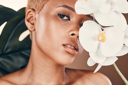 Flower, portrait and black woman with cosmetics, dermatology and treatment for wellness and confidence. Face, female and lady with plant, orchid and natural care for luxury, healthy and smooth skinの写真素材