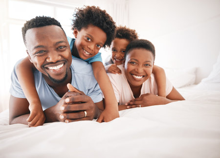 Happy, bonding and portrait of a black family on a bed for playing, quality time and comfort. Smile, love and African children with parents in the bedroom for happiness, relaxation and stress reliefの写真素材