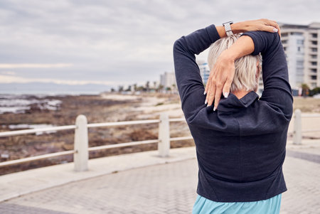 Back of woman, exercise and stretching at beach promenade for fitness, wellness and mockup. Lady, runner and person warm up arms at ocean for outdoor workout, sports action and healthy cardio runningの写真素材